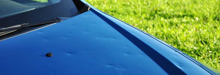 Hail dents visible on a blue vehicle body panel